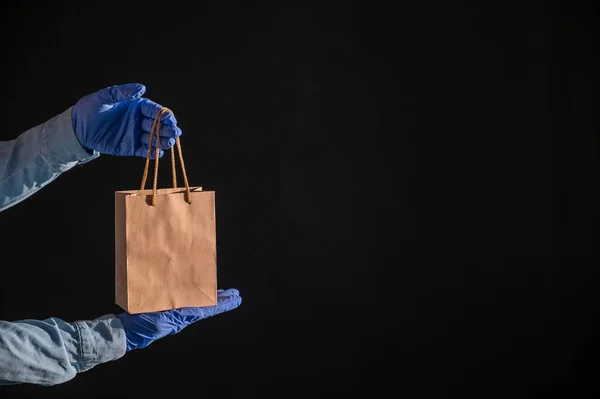 Express-Lieferung an die Coronavirus-Epidemie. Großaufnahme von Kurieren mit Gummihandschuhen und einer Papiertüte mit Griffen. Verpackungen aus umweltfreundlichem Recyclingmaterial. Spende für Quarantäne. — Stockfoto