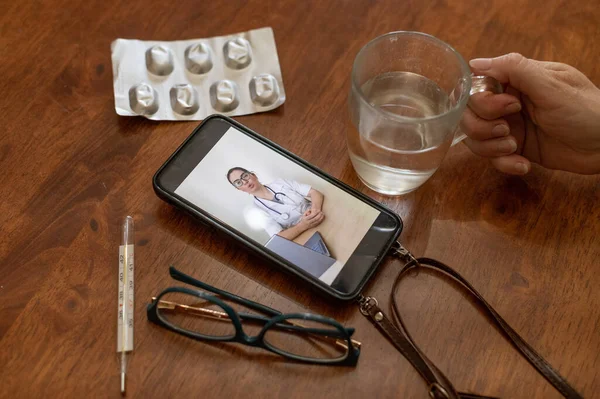 Online consultation. The doctor talks to the patient on a video call. An elderly woman has the flu. A quarantined pensioner communicates with her doctor by phone. Hands of an old woman.