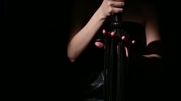 BDSM concept. A woman in a leather dress holds a black whip with a long fringe. Role-playing games for adults. Close-up of sex toys for domination. — Stock Video