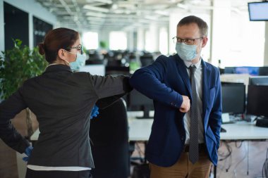 Ofis çalışanları dirsek tokuştururken el sıkışıyorlar. Koronavirüsün yayılmasını engellemenin yeni bir yolu. Koruyucu maskeli kadın ve erkek iş yerinde sosyal mesafeyi koruyor..