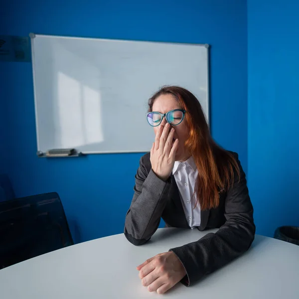 Eine Frau in Anzug und Brille gähnt im Konferenzraum. Eine Bürokauffrau mit chronischer Müdigkeit sitzt an einem Tisch in einer langweiligen Werkstatt. Partner kommen zu spät zum Geschäftstreffen. — Stockfoto