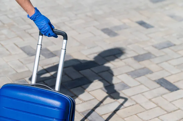 Close-up van een vrouwelijke hand in een handschoen op een handvat. Er loopt een vrouw op straat met een grote blauwe tas. Reisconcept tijdens een virusuitbraak. Persoonlijke hygiëne — Stockfoto