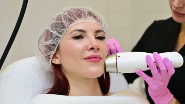 Het handvat van het radiofrequentieapparaat op de kin van een vrouwelijk gezicht tijdens een schoonheidsbehandeling van de huid. Beautician maakt een hardware facelift van een vrouw gezicht — Stockvideo