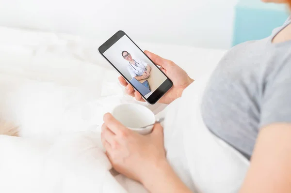 Elinde akıllı bir telefonla hastalık izninde olan bir kadın. Bir grip hastası tıbbi video blogu izliyor. Doktor telefonla çevrimiçi bir danışma yürütüyor. Yatak istirahatı. — Stok fotoğraf
