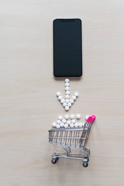 Online pharmacy concept. Buying medicine online over the phone. Delivery of pharmaceuticals. Mini trolley with capsules and a smartphone with a black blank screen.
