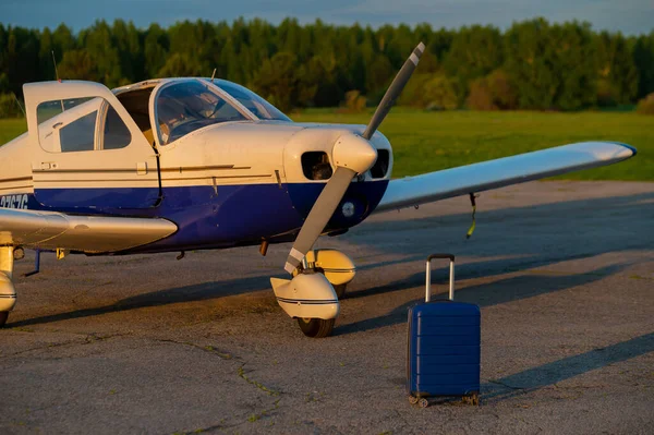 Una maleta azul y un pequeño jet privado. Avión de cuatro plazas con una hélice para el taxi aéreo. Concepto de auto viaje. Avión para personas VIP . — Foto de Stock