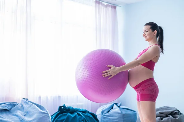 En gravid kvinna i sportkläder gör gymnastik för gravida kvinnor. Flickan är engagerad i fitness med en boll för förväntansfulla mödrar. Sista trimestern. — Stockfoto