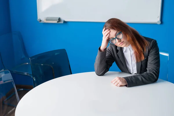 Una mujer de negocios cansada con gafas y un traje sola en una sala de conferencias vacía. Un oficinista con dolor de cabeza espera a que comience la presentación en la sala de juntas. — Foto de Stock