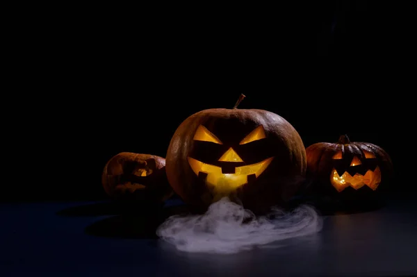 Tarjeta de Halloween. jack o linterna con velas brillan sobre un fondo negro. Una fila de calabazas espeluznantes con muecas talladas fuma en la oscuridad. —  Fotos de Stock