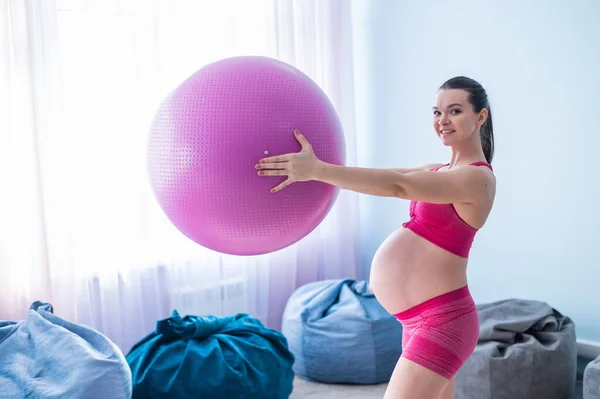 Een zwangere vrouw in sportkleding doet gymnastiek voor zwangere vrouwen. Het meisje is bezig met fitness met een bal voor aanstaande moeders. Laatste trimester. — Stockfoto