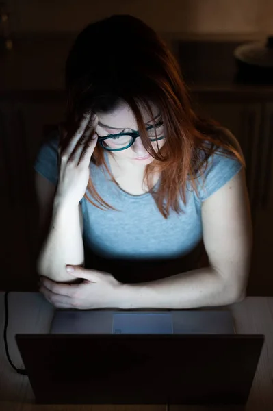 Femme rousse fatiguée dans des lunettes travaillant sur un ordinateur portable. La fille à l'ordinateur avec une migraine tient la main au temple. Échec au travail. Femmes travaillant des heures supplémentaires — Photo