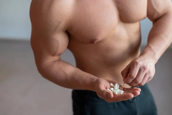Body builder sans visage boit des capsules d'hormone de croissance. Un gros plan d'un homme musclé avec un torse nu contient une poignée de vitamines et de suppléments de fitness . — Photo