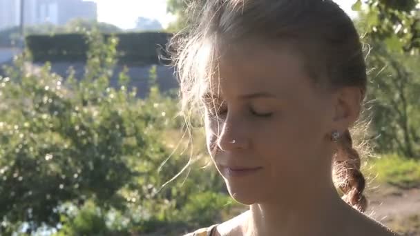 Mujer atractiva se sienta con los ojos cerrados en el verde parque de verano al aire libre . — Vídeos de Stock