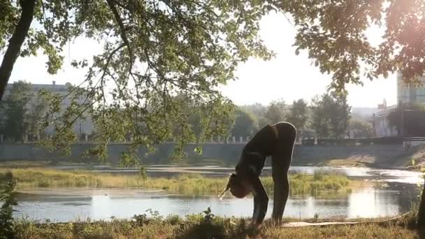 Mujer en el parque de la ciudad realiza diferentes asanas de yoga sobre una esterilla . — Vídeo de stock