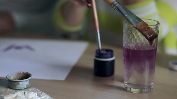 Los cepillos están siendo lavados en el vaso de agua y sumergidos en el color púrpura . — Vídeos de Stock