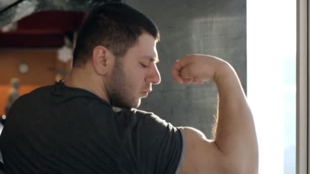 Γκρο πλαν αξύριστος bodybuilder εξετάζει δικέφαλου του στα χέρια στο γυμναστήριο. — Αρχείο Βίντεο