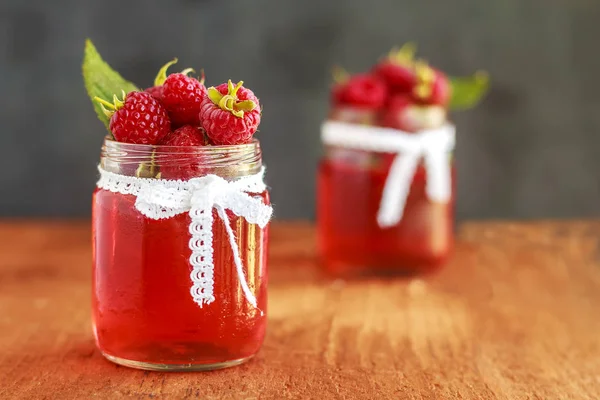 Rustic fresh ripe raspberry jam in glass bottles with leaves on brown background. Copy space. Close up. Front view. — Stock Photo, Image