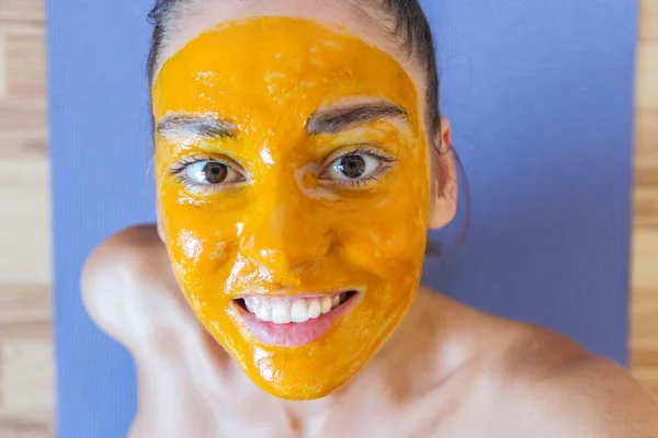 Лицо улыбающейся девушки рядом с оранжевой маской куркумы — стоковое фото