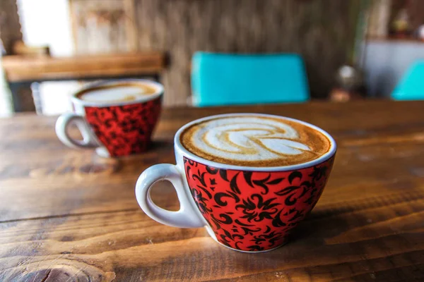 Two red coffee cups with milk foam on wooden table