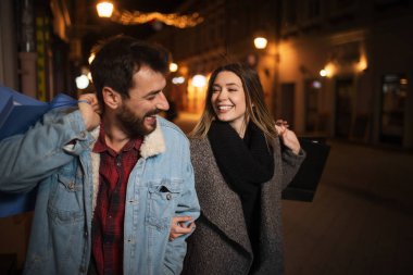 Geceleri şehirde alışveriş yapan genç bir çiftin fotoğrafını çek.