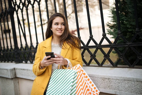 Mujer con un abrigo amarillo usando móvil — Foto de Stock