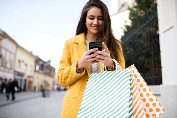 Mujer con un abrigo amarillo usando móvil — Foto de Stock