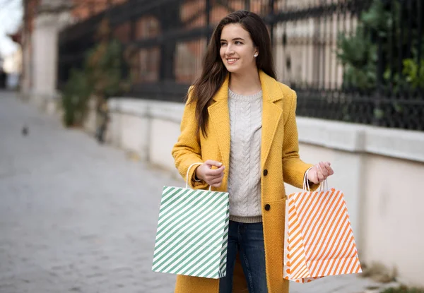 Mujer sonriente con un abrigo amarillo, mantener bolsas de compras — Foto de Stock