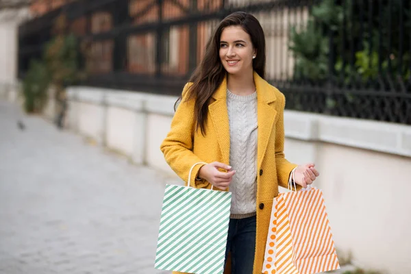 黄色のコートで笑顔の女性,ショッピングからバッグを保持 — ストック写真
