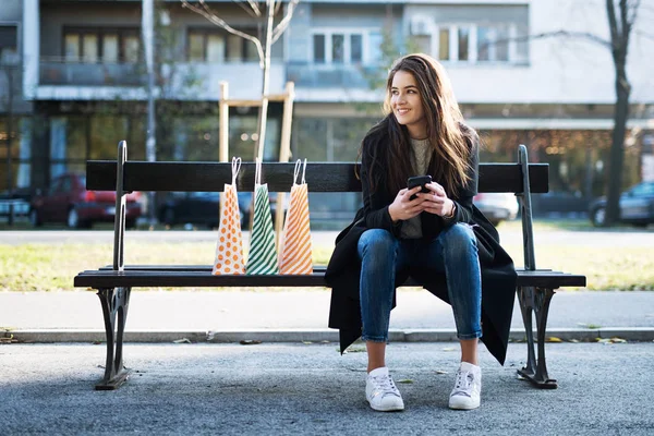 Hermosa chica sentada en el banco y el uso de móviles — Foto de Stock