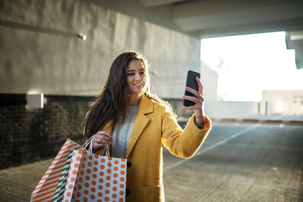 Νεαρή γυναίκα που χρησιμοποιεί κινητό μετά τα ψώνια — Φωτογραφία Αρχείου