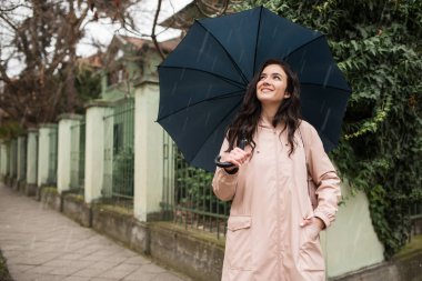 Elinde şemsiyesi olan genç bir kız yağmurda duruyor ve gökyüzüne bakıyor.