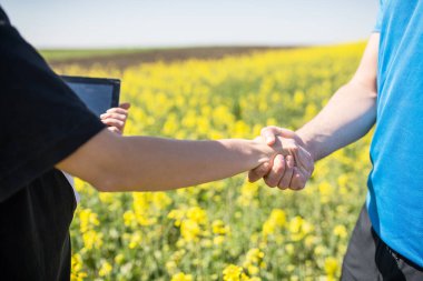 İki genç tarımcı başarıyla bir saha işi ayarladı ve el sıkışıyorlar. Kolza üretiminde başarılı bir anlaşma.