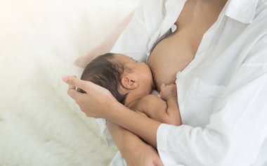 Genç Asyalı anne, sevimli bebeğini evdeki oturma odasında emziriyor. Anne sevgisi, koşulsuz sevgi, Anneler Günü, Kadınlar Günü konsepti..