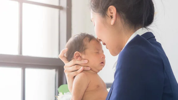 Young pretty mom kissing adorable little baby boy in the office. Single mother taking care of newborn child at the work place. Business, mom and baby, women\'s day, mother\'s day concept.