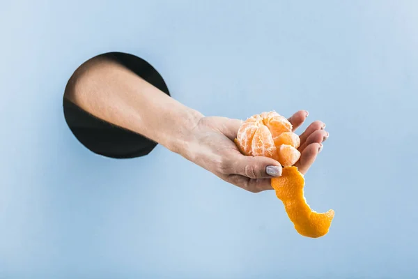 A woman\'s hand pulls a half-peeled tangerine out of a black hole