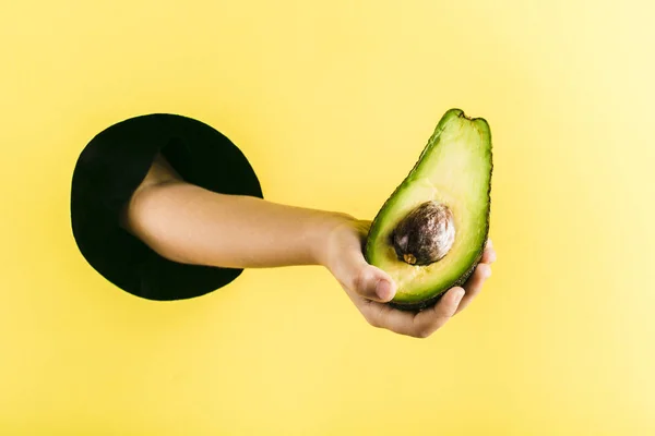A child's hand pulls an avocado out of a black hole in a yellow