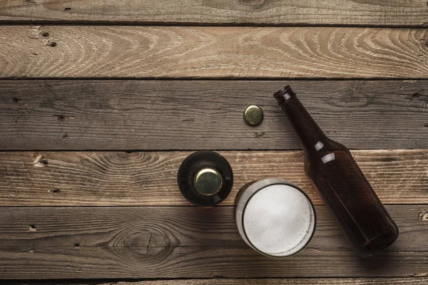 Two dark beer bottles and a glass of beer and foam on a wooden background. Top view. Copyspace. Horizontal orientation.