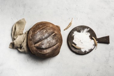 Yuvarlak bir somun ekmek, üzerinde gri keten peçete, üzerinde un ve buğday dikenleri olan bir tahta bulunan bir tahta üzerinde yatar. Kopyalama alanı ile üst görünüm. yatay yönelim