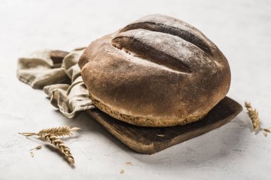 Hafif arka planda gri keten peçeteyle ahşap bir tahtanın üzerinde yuvarlak bir somun ekmek. Kopya alanı ile yakın çekim. yatay yönelim