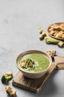 Kremalı brokoli çorbası, açık gri bir zemin üzerinde tahta bir tabakta kızarmış ekmek. Sağlıklı beslenme kavramı. Kopyalama alanı ile kapatın. Dikey yönelim.