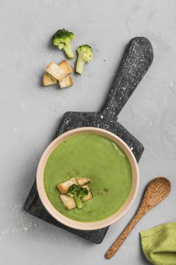 Kremalı brokoli çorbası, açık gri bir zemin üzerinde tahta bir tabakta kızarmış ekmek. Sağlıklı beslenme kavramı. Kopyalama alanı olan üst görünüm. Dikey yönelim.