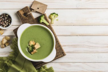 Brokoli kremalı çorba, servis tabağında beyaz bir tabakta kızarmış ekmek ve hafif ahşap arka planda yeşil bir peçete. Sağlıklı beslenme kavramı. Kopyalama alanı olan üst görünüm. Yatay yönelim.