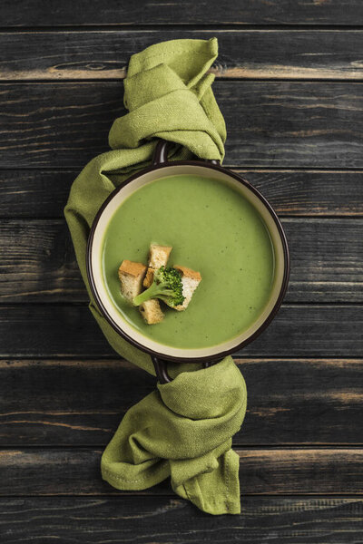 Broccoli cream soup with croutons in a plate with a green napkin on a wooden black background. Concept of healthy nutrition. Top view with copy space. Vertical orientation.