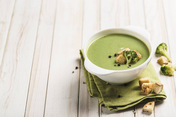 Cream broccoli soup with croutons in a white plate on a green napkin on a light wooden background. Concept of healthy nutrition. Close up with copy space. Horizontal orientation.