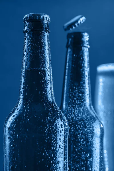 Two dark fogged beer bottles and a glass of beer and foam on a classic blue background. flying cover. Closeup. Copyspace. Vertical orientation.