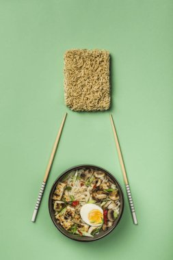 Mantarlı erişte kasesi, yumurta, tofu peyniri, yemek çubukları ve yeşil arka planda malzemeler. Asya yemekleri konsepti. Kopyalama alanı ile üst görünüm. Dikey yönelim.