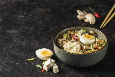 Mantarlı erişte kasesi, yumurta, tofu peyniri, yemek çubukları ve koyu arkaplanda malzemeler. Asya yemekleri. Kopyalama alanı ile kapatın. Yatay yönelim.