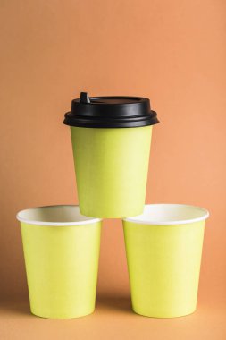 Turuncu arka planda kapalı siyah kapaklı, yeniden kullanılabilir yeşil kahve fincanları. Fotokopi alanına sıfır atık konsepti. Dikey yönelim.