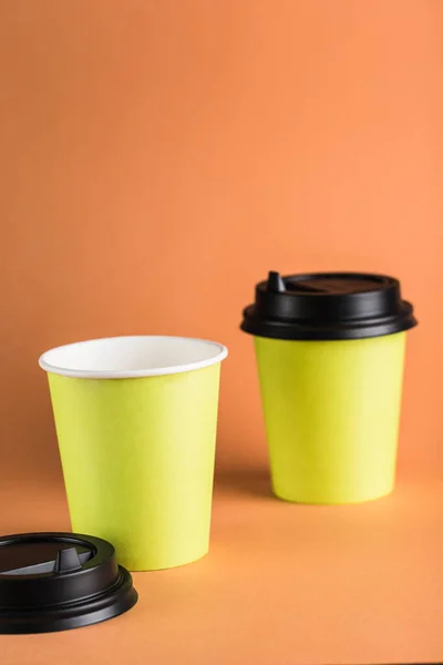 Some green paper reusable coffee cups with a closed black lid on an orange background. Zero waste concept close-up with copy space. Vertical orientation.
