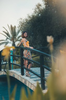 Tropiklerde tatilde bir köprüde duran palmiye ağaçları arasında poz veren kız mankeni. Deniz kenarındaki sıcak bir ülkede tatil. Kopyalama alanı ile dikey yönelim.